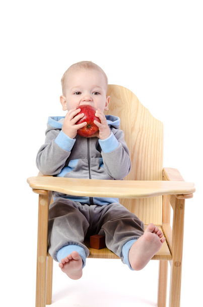 Jongetje met rode appel zit in kinderstoel geïsoleerd op w - Foto, afbeelding