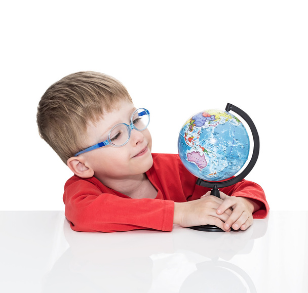 The five-year-old boy in blue points sits at a white table and holds the globe in hand - Foto, immagini