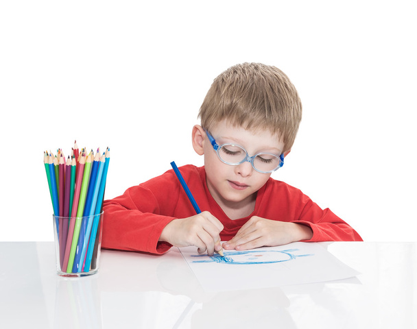 The five-year-old boy in blue points sits at a white table and and draws pencils - Fotografie, Obrázek