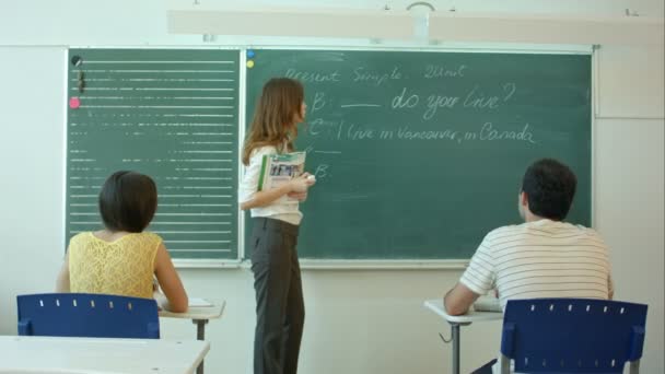 Jonge leraar in de buurt van schoolbord in school klas praten met klasse - Video