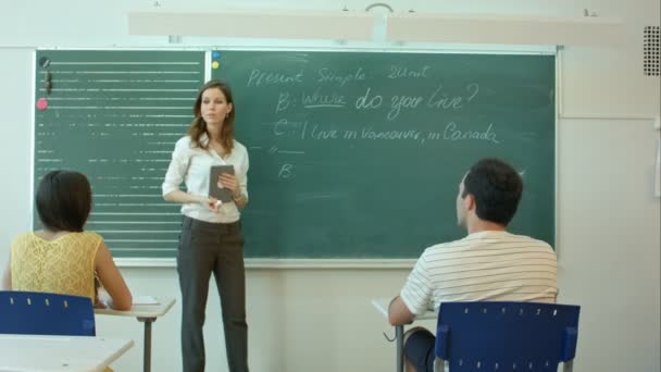 Jonge vrouwelijke leraar schrijven op schoolbord in de klas - Video