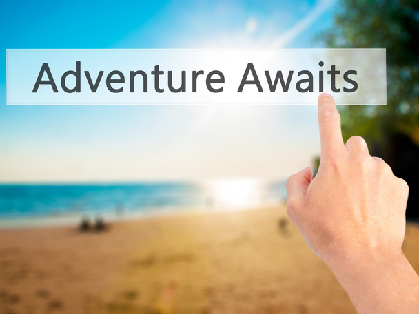Adventure Awaits - Hand pressing a button on blurred background  - Фото, изображение