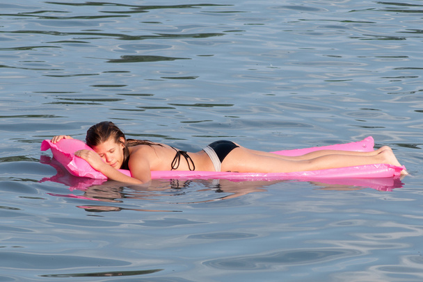 Милая девушка-подросток лежит на розовом матрасе, который плавает на поверхности моря
 - Фото, изображение
