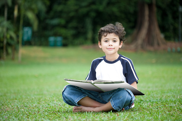 Young boy enjoying his reading book in outdoor park - Фото, изображение