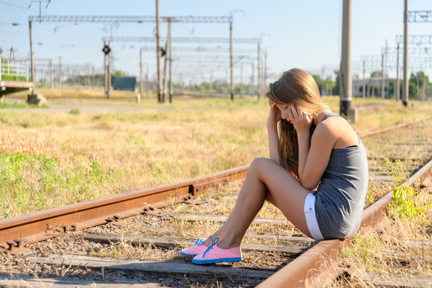 Boos tiener meisje zittend op spoorbaan op het platteland - Foto, afbeelding