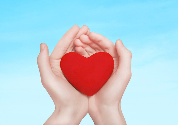 Open hands holding showing red heart over blue sky background - Foto, Imagem