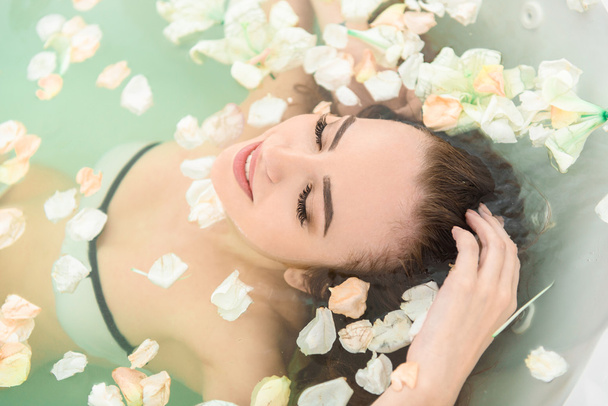 Happy young woman luxuriating in water with petals - Fotografie, Obrázek