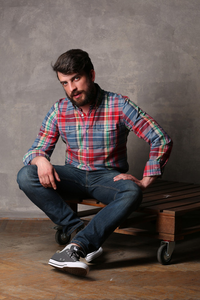 Bearded man in colorful shirt sitting on a wooden board - Foto, afbeelding