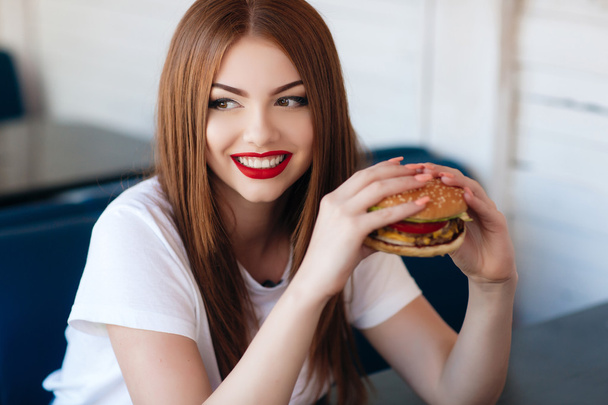 Lady with a hamburger for a table in a cafe - Фото, изображение