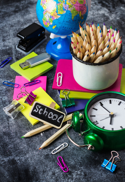 Papelería escolar, lápiz, pluma, nota, reloj despertador en pizarra grunge
 - Foto, imagen