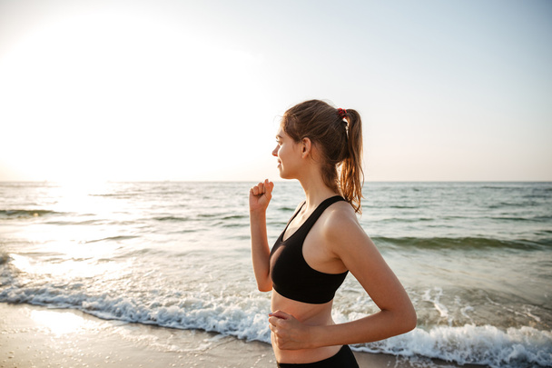 Seitenansicht einer gesunden jungen Frau, die am Strand läuft - Foto, Bild