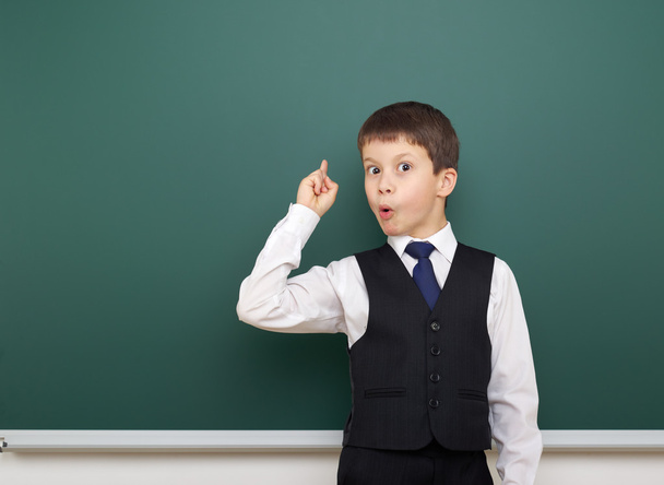 school student boy posing at the clean blackboard, show finger up and point, grimacing and emotions, dressed in a black suit, education concept, studio photo - Photo, Image