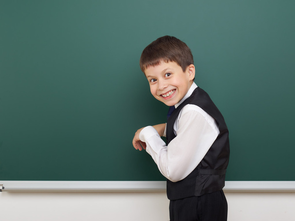 school student jongen die zich voordeed op de schone blackboard, grimassen en emoties, gekleed in een zwart pak, onderwijs concept, studio foto - Foto, afbeelding