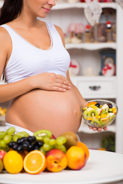 Close-up of a pregnant  tummy with fresh fruit and plate of salad. Healthy pregnancy, diet and vitamins - 写真・画像
