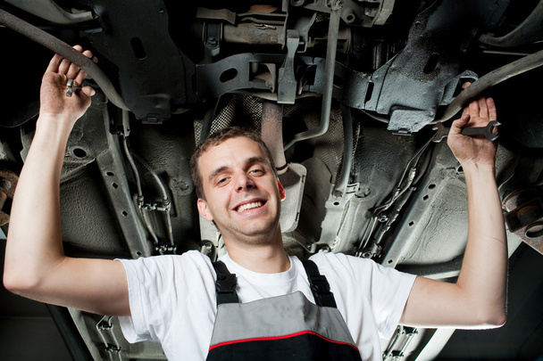 młody mechanik praca pod samochód i uśmiechając się - Zdjęcie, obraz