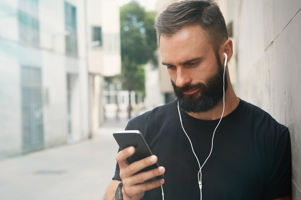 Bearded Muscular Man Wearing Black Tshirt Blank Snapback Cap Summer Time.Young Men Using Smartphone Headphones Looking Screen Smiling.Horizontal. Color Filter. - Foto, Bild