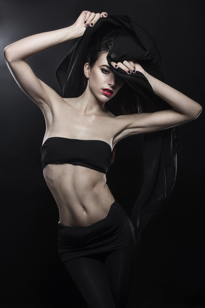 Jovem moda modelo grego-americano segurando um tecido preto soprado pelo vento isolado em estúdio preto tiro
 - Foto, Imagem