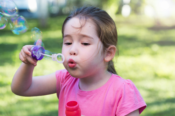 A little girl blowing soap bubbles in a park - Zdjęcie, obraz