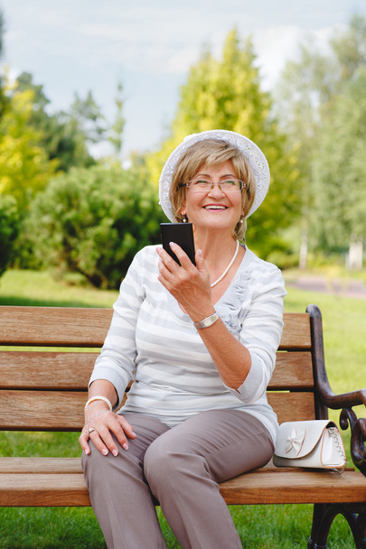 Houkutteleva kypsä nainen käyttää älypuhelinta puistossa
 . - Valokuva, kuva