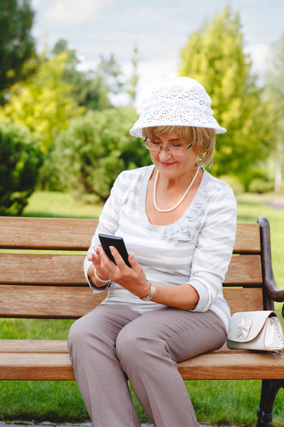 Attractive mature woman using smartphone in a park . - Foto, imagen