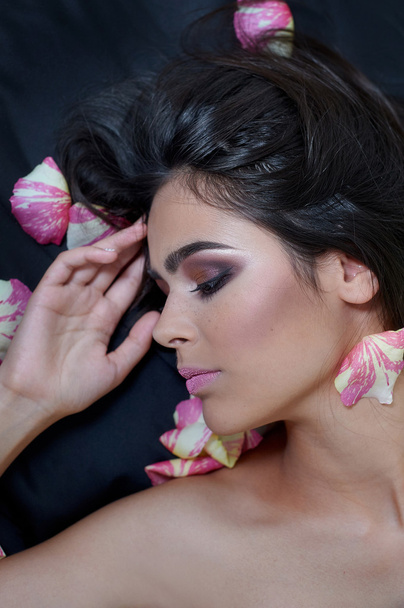 Portrait of a beautiful young woman laying on sparse rose petals - Foto, imagen