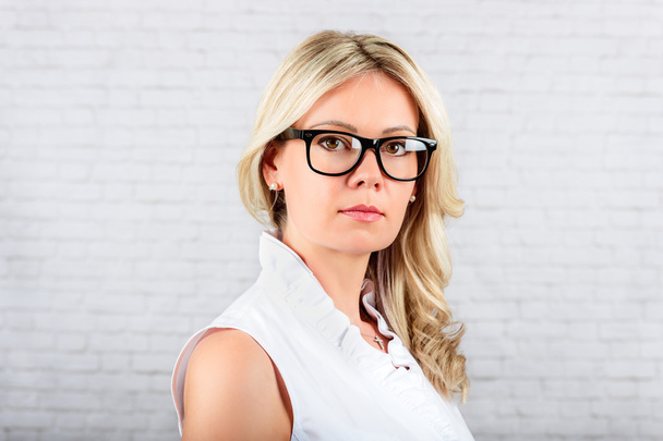 れんが造りの白い背景に立っている眼鏡を身に着けている若いブロンド女性のスタジオ ポートレート - 写真・画像