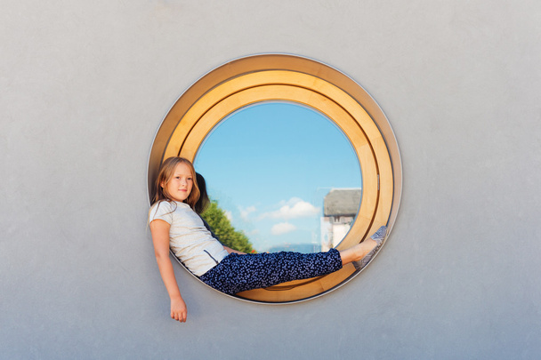 Αστείο, μικρό κορίτσι που κάθεται σε ένα παράθυρο γύρο σε εξωτερικούς χώρους - Φωτογραφία, εικόνα