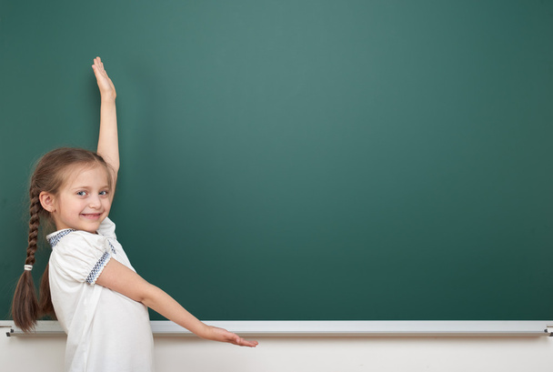 school student girl posing at the clean blackboard, grimacing and emotions, dressed in a black suit, education concept, studio photo - Fotoğraf, Görsel