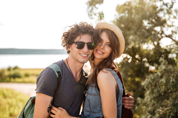 Portrait of smiling hipster couple standing against trees and sea - Fotografie, Obrázek