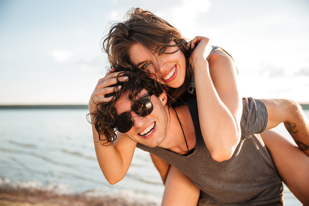 Man giving piggyback ride to girlfriend by the ocean - Photo, image