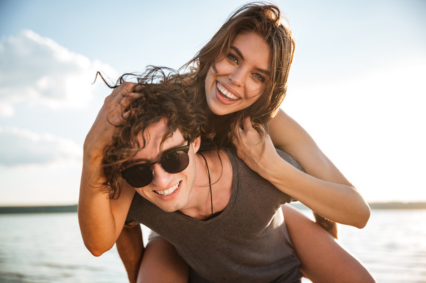 Young happy couple piggyback at the beach - 写真・画像