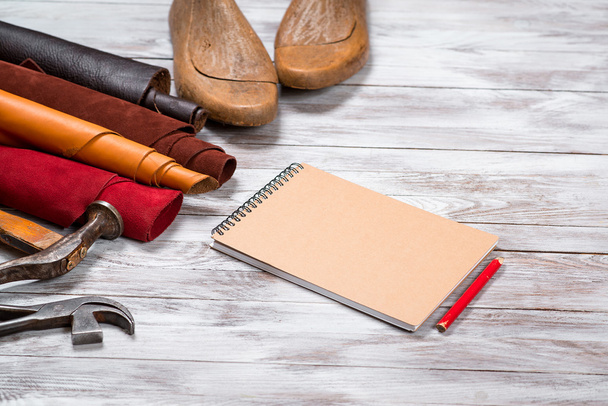 Brightly colored leather in rolls, working tools, shoe lasts, notebook with pencil on white background. Leather craft. - Photo, Image