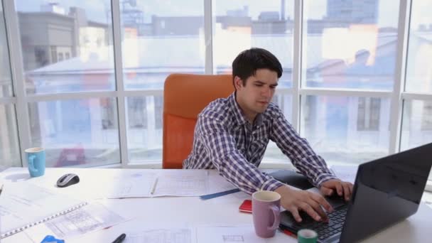 Young architect, businessman in modern bright office working on computer with blueprint and plans. - Footage, Video