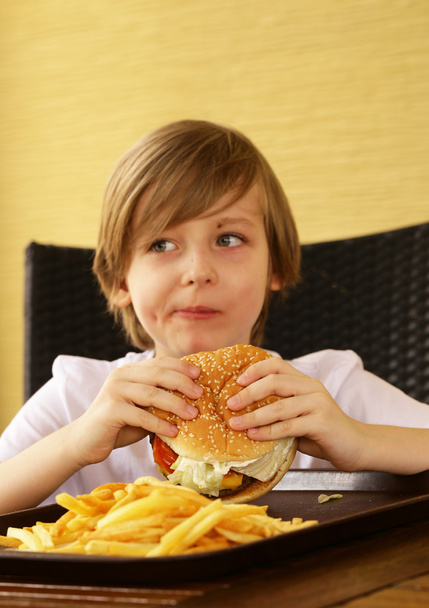 ładny blond chłopiec jedzenie hamburger i frytki - Zdjęcie, obraz