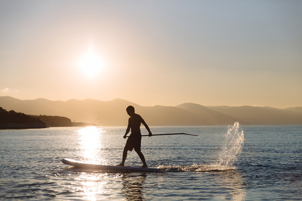 silhouette of young boy paddle boarding at sunset. concept  lifestyle sport - Fotoğraf, Görsel