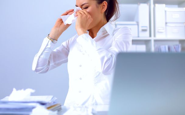 Young businesswoman blowing her nose, sits at the desk - Фото, изображение