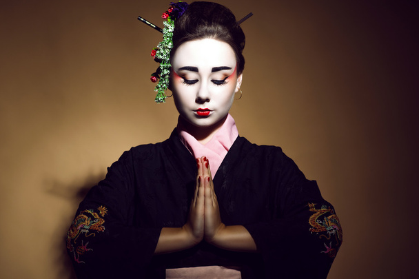 Portrait of young heisha in kimono welcoming with traditional folded hands. - Foto, Imagen