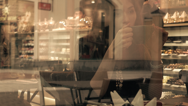 Gyönyörű barna lány iszik forró csokoládé cukrászda. Nézd, az ablakon kívül. 4k videóinak - Felvétel, videó