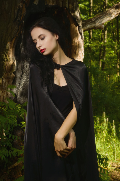 Όμορφη μελαχρινή γυναίκα στο μαύρο φόρεμα και μαύρο μανδύα στο μ - Φωτογραφία, εικόνα