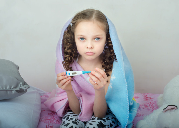 Cute little ill girl with a thermometer on her bed. - Foto, imagen