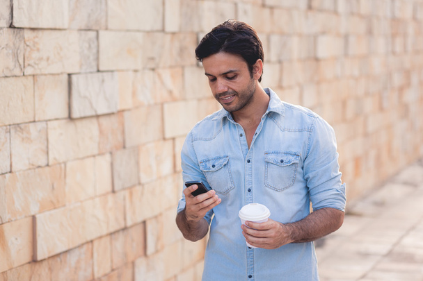 Portrait of young man drinking coffee on the street while using mobile phone - Foto, Imagem