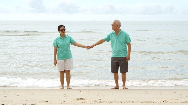 海沿いのビーチで一緒に歩くアジア シニア カップル - 写真・画像