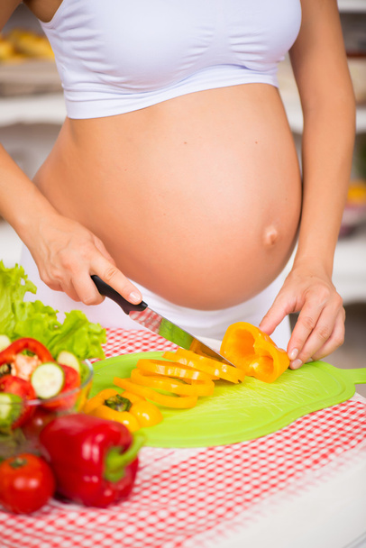 Close-up of a pregnant belly. Pregnant woman in the kitchen preparing a vegetable salad. - Fotoğraf, Görsel