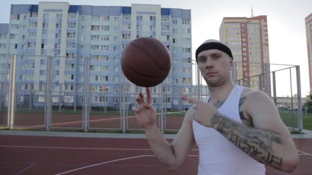 Spinning egy ujját a kosárlabda, a férfi a kerületi sport földön háttér lakóépületek. - Felvétel, videó