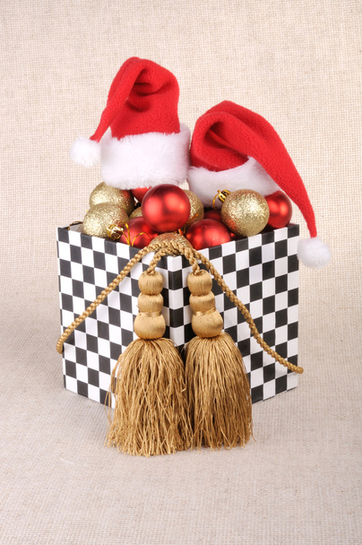 caja de regalo en estilo dominó, llena de bolas de Navidad. Sombreros Santa Claus.Decoración hecha de cordones de oro con borlas
. - Foto, Imagen
