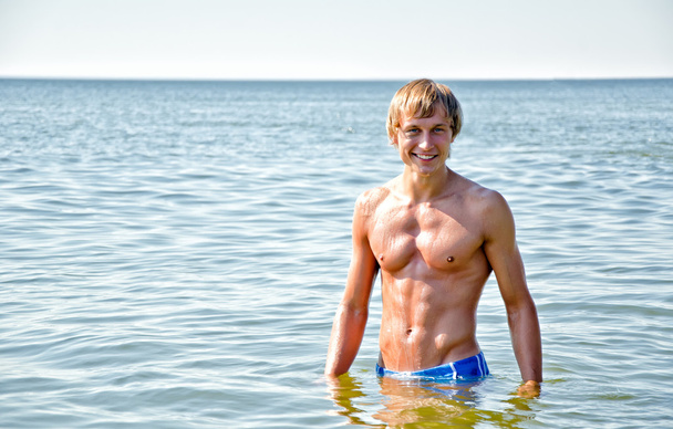 Полуобнаженный красивый улыбающийся мужчина, стоящий в море
 - Фото, изображение
