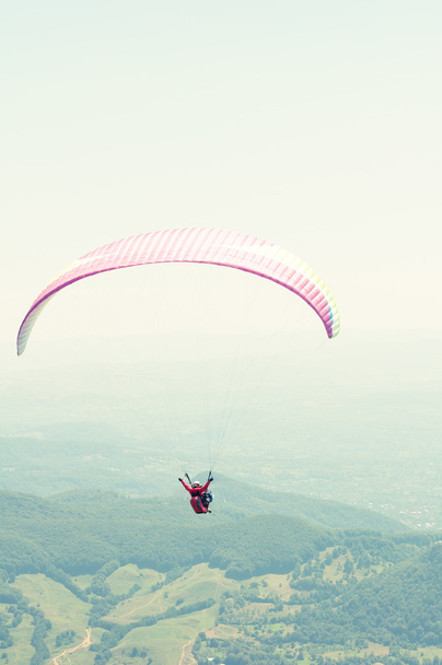 Parapente voando sobre as colinas verdes
 - Foto, Imagem