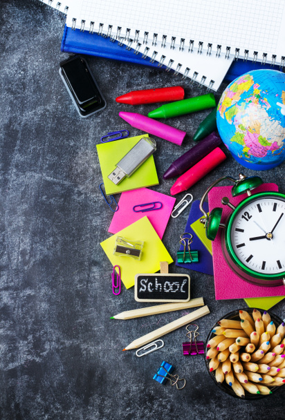 Papelería escolar, lápiz, pluma, nota, reloj despertador en pizarra grunge
 - Foto, Imagen