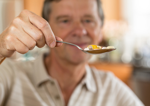 Homme âgé mangeant une cuillère de vitamines
 - Photo, image