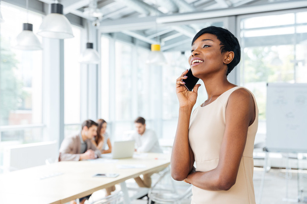 Cheerful businesswoman standing and talking on mobile phone in office - Foto, Imagen